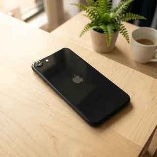Refurbished black iPhone SE in use, showing someone holding the compact phone, with a coffee cup in the background.