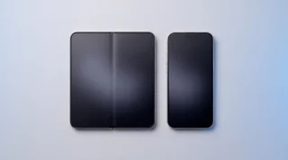 An iPhone Duo standing half open like a book on a pale grey studio surface, its inner folding screen showing the fault owners are reporting: a dark dead patch at the hinge, a thin line up the crease and a bright stripe of stuck pixels across the right half