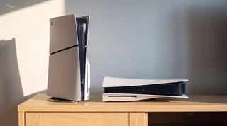 A PlayStation 5 lying flat on a pale oak media unit in warm summer sunlight, with clear space around it