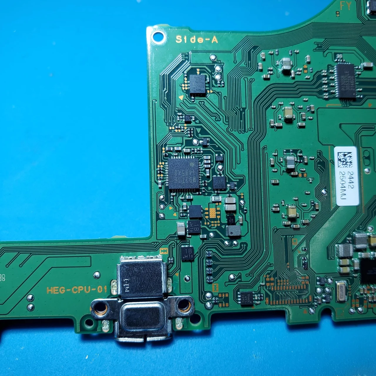 A real Nintendo Switch OLED circuit board, marked HEG-CPU-01, on a blue bench mat, showing the silver USB-C port and the power circuit around it