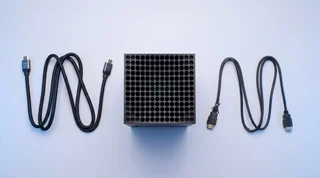 A single Xbox Series X console standing upright on a clean pale-grey studio surface with an HDMI cable connected at the base and a subtle blue glow at the connection point