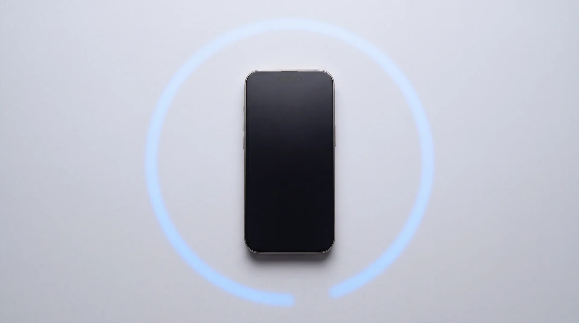 A single iPhone 15 Pro lying flat on a clean pale-grey studio surface with its screen dark, an unfinished arc of blue light curving around it on the background like a countdown