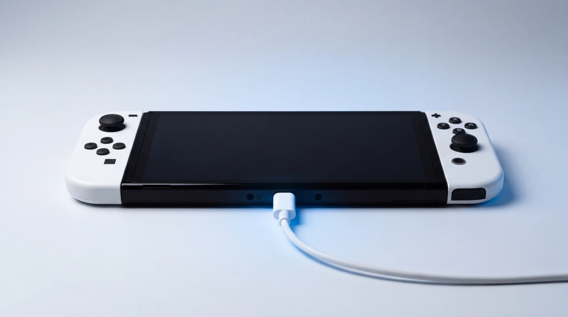 A white Nintendo Switch OLED lying flat with its screen off and a USB-C charging cable plugged into the port on its bottom edge, a soft blue glow at the connection