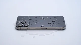 A modern iPhone covered in water droplets, lying in a small pool of water on a clean studio surface